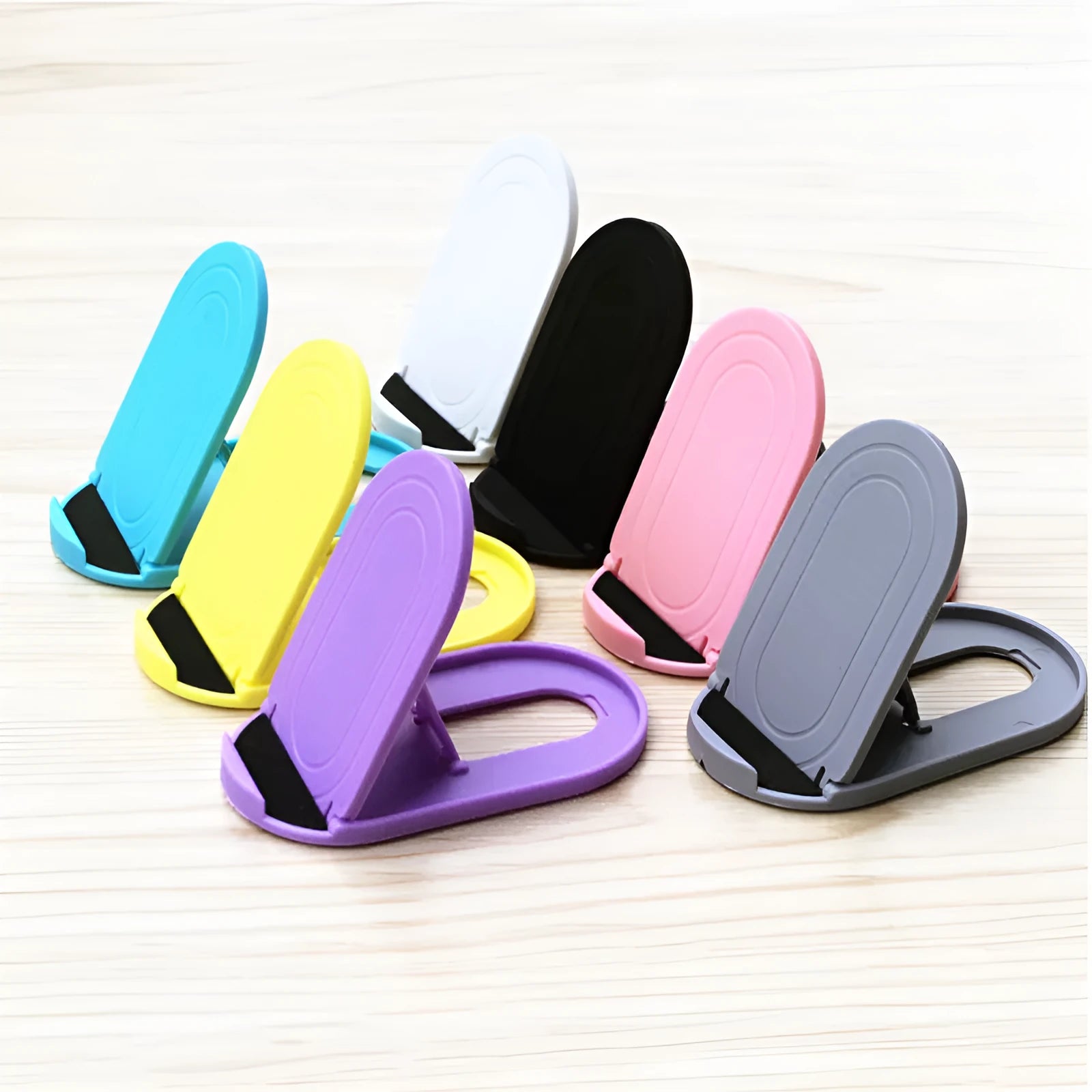 Adjustable plastic mobile phone stand in multiple colours on a table, holding a smartphone at an angle