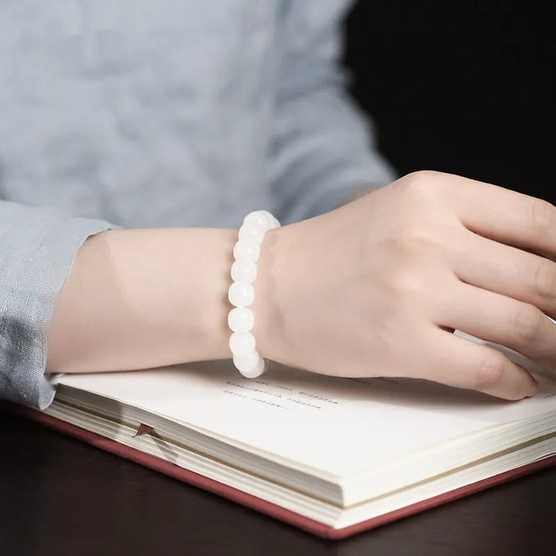 White Hetian jade barrel bead bracelet on a wrist, showing smooth oval beads on a string.