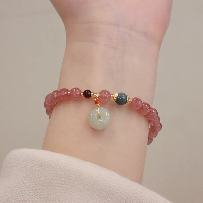 Women's strawberry quartz bracelet with gold purse-shaped safety buckle and lucky bag charm on geometric beads.