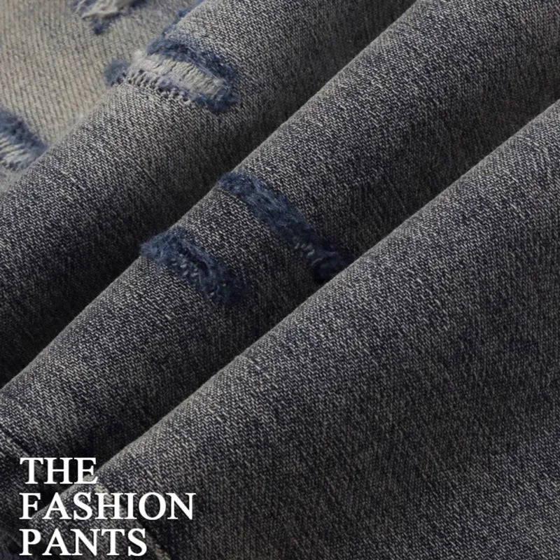 Man wearing slim fit distressed blue jeans with hole patches and embroidered details on the legs.