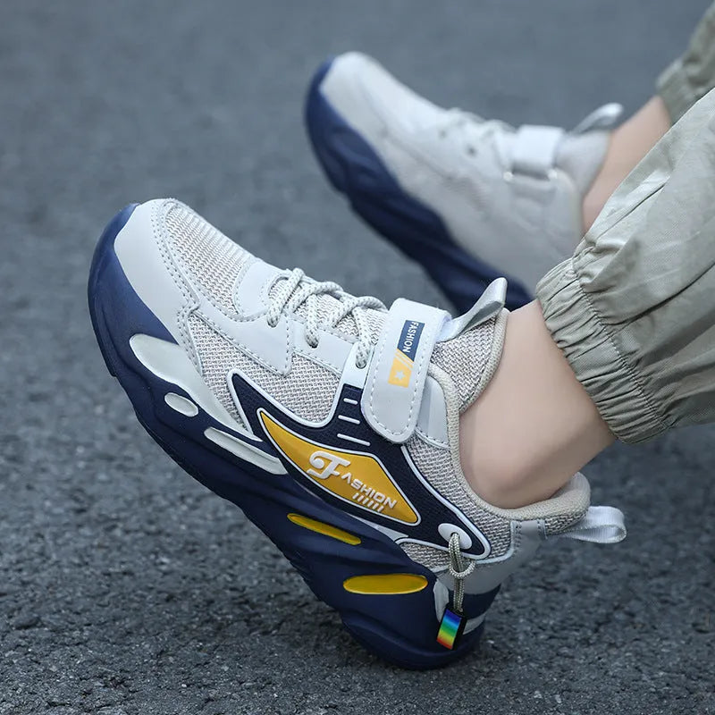 Boys sports running shoes in dark blue with a mesh upper and Velcro strap, shown on a hard ground surface.