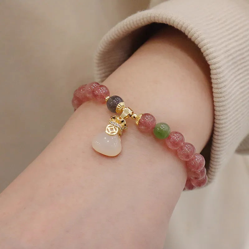 Women's strawberry quartz bracelet with gold purse-shaped safety buckle and lucky bag charm on geometric beads.