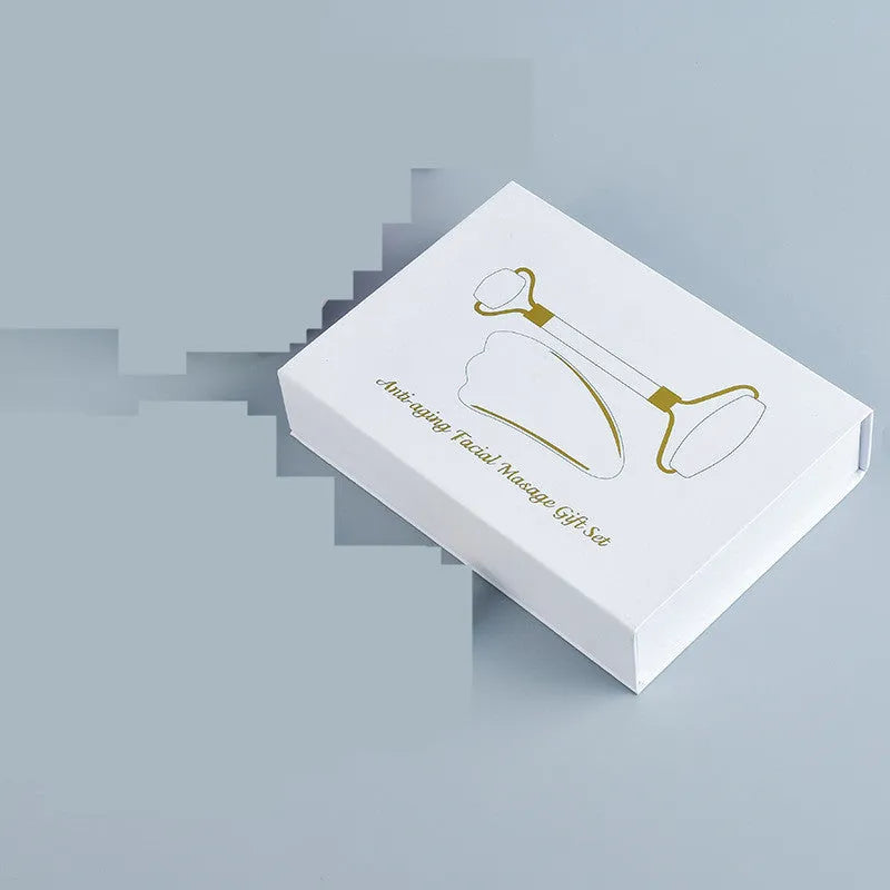 White jade facial roller set with double-headed roller, claw tool, and gua sha board on a wooden table.