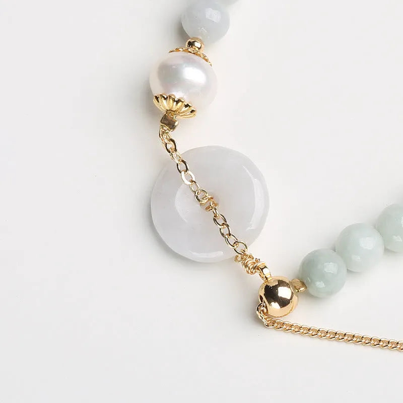 Close-up of a women's bracelet with a jade peace symbol buckle on a string of freshwater pearls.