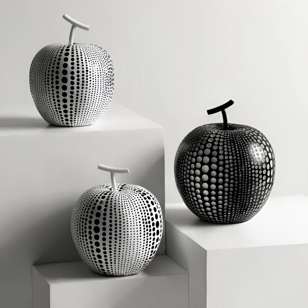 Decorative resin apple and pear crafts in white, orange, black, and blue on a shelf.