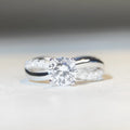 A geometric twisted silver ring with a 1 karat moissanite stone in a four-claw setting.