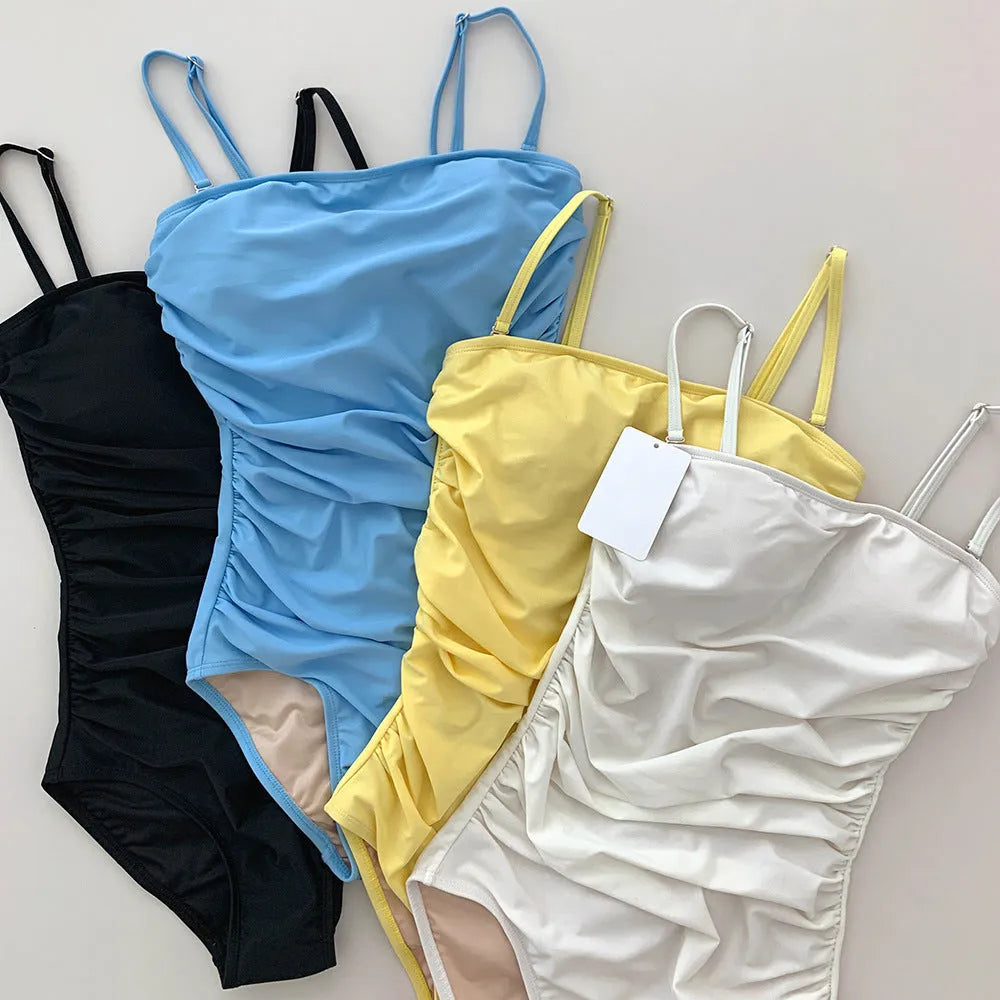 Sling style one-piece swimsuit with belly pleating in blue, white, yellow or black solid colours