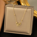 Gold electroplated women's bow necklace with cross chain design on white background
