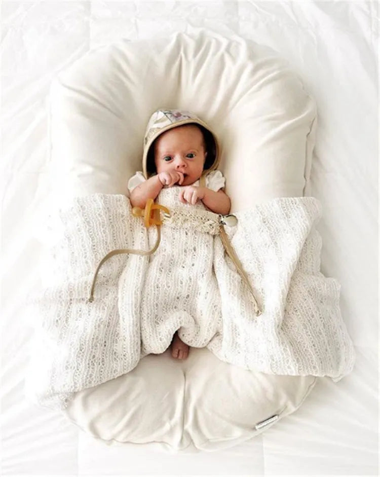 Beige portable cotton baby nest crib for newborns on a neutral background