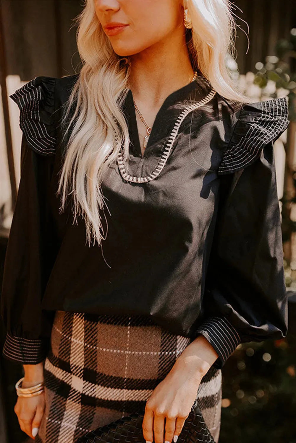 Black long sleeve V-neck blouse with contrast stitching and three-quarter ruffle sleeves.