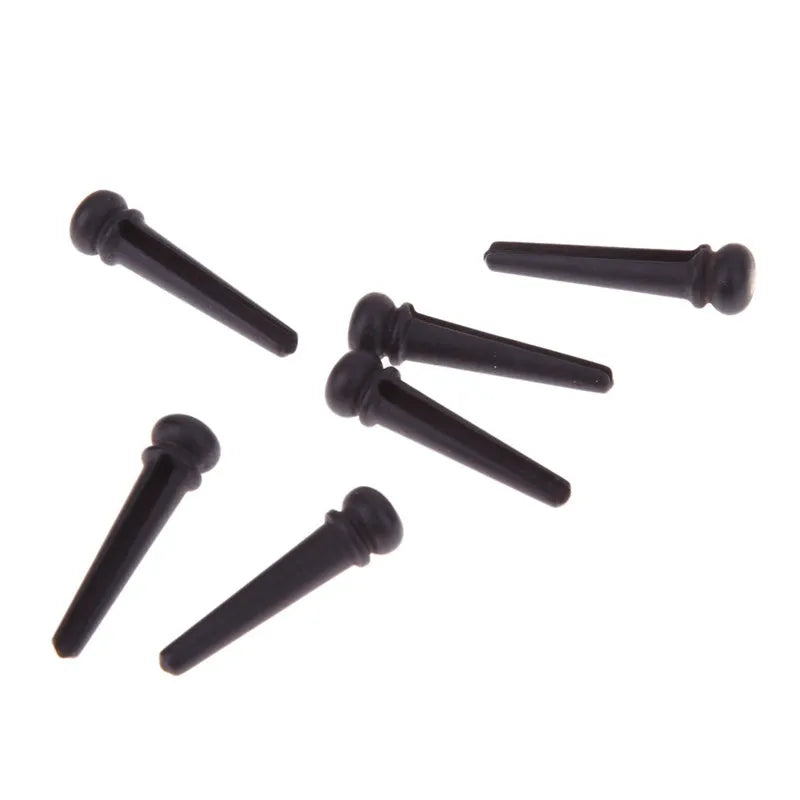 Six matt black ebony folk guitar string nails on a grey background