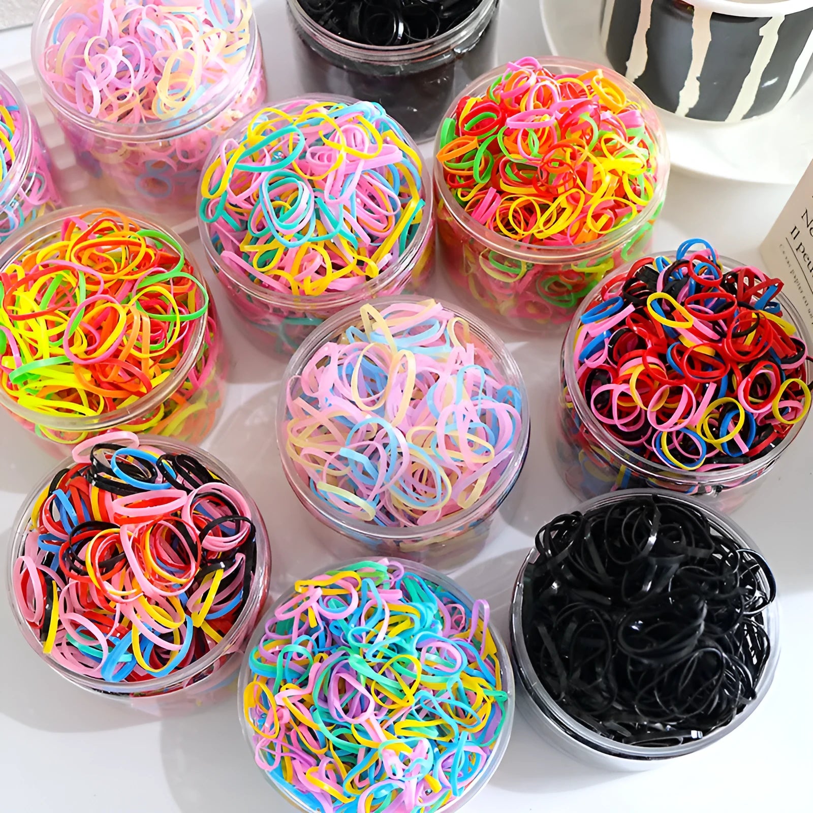 Multi-colour TPU baby hair elastic bands spilling from a reusable container.
