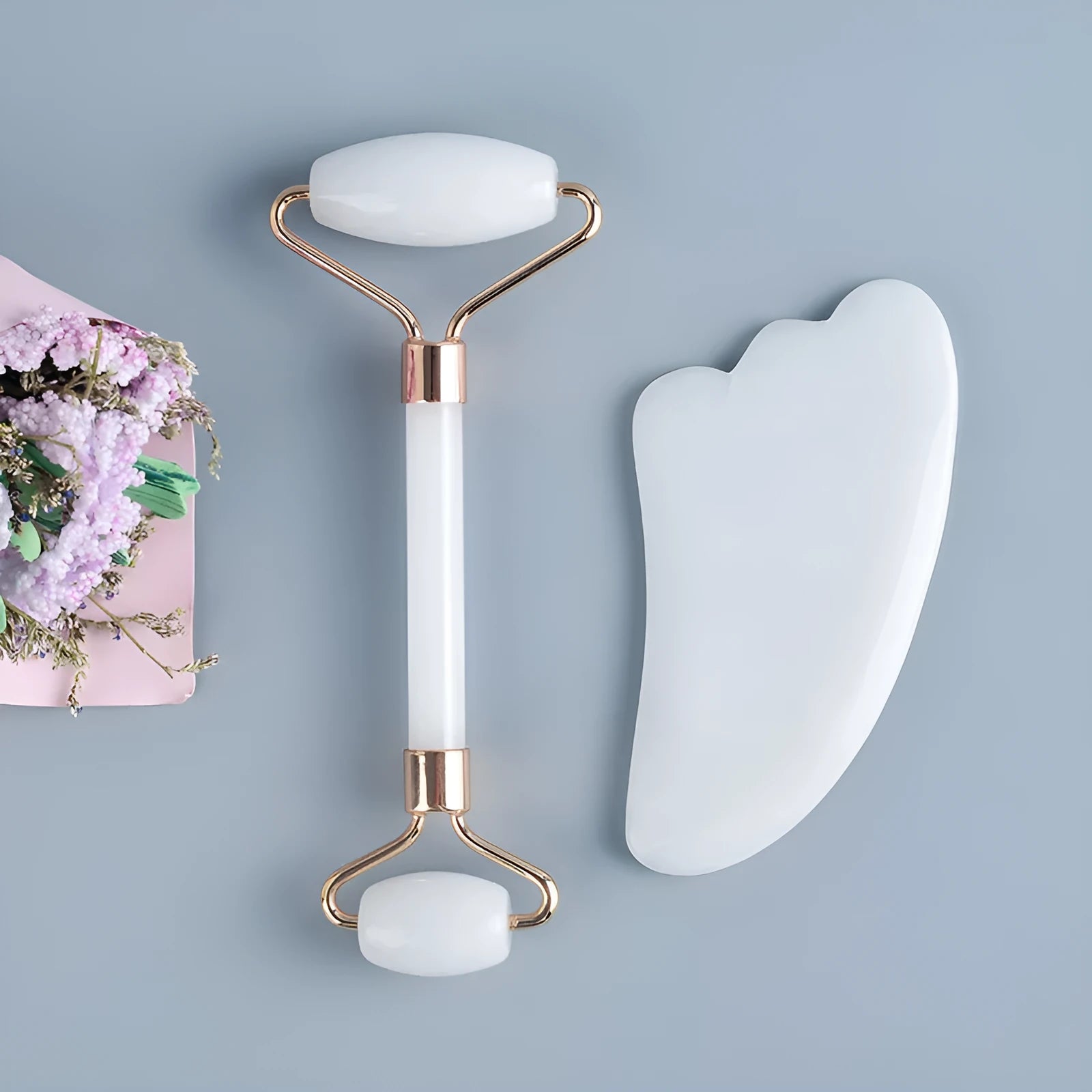 White jade facial roller set with double-headed roller, claw tool, and gua sha board on a wooden table.