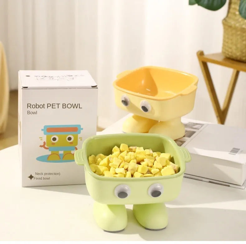 Green cartoon robot-shaped elevated cat bowl with tilted design and non-slip base on a table.