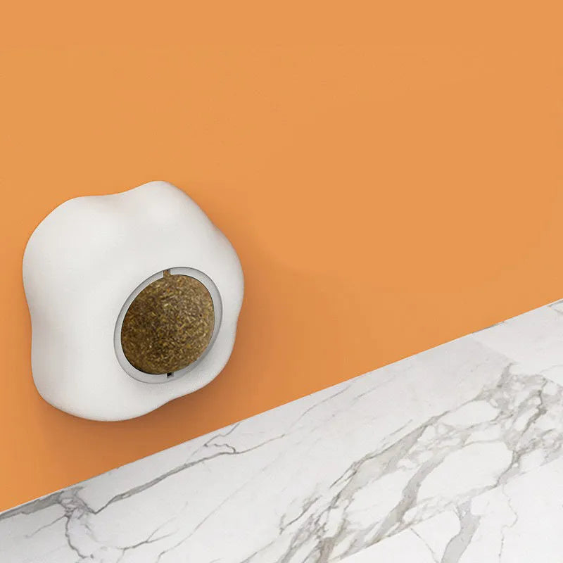 Soft plush catnip ball toy with adhesive base sticking to a wall for interactive feline play