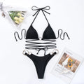 Black women's bikini set with metal ring detail and long criss-cross straps on a solid colour background.