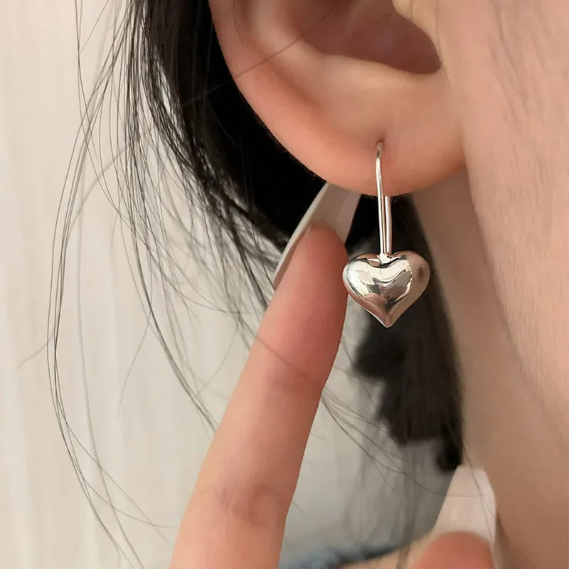 Silver-toned heart-shaped women's earrings with glossy finish and matching heart-shaped ear hooks.