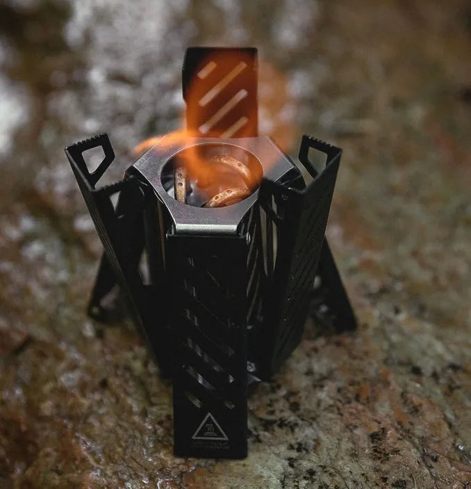 Black hexagon alcohol camping stove with foldable design shown next to ruler for scale