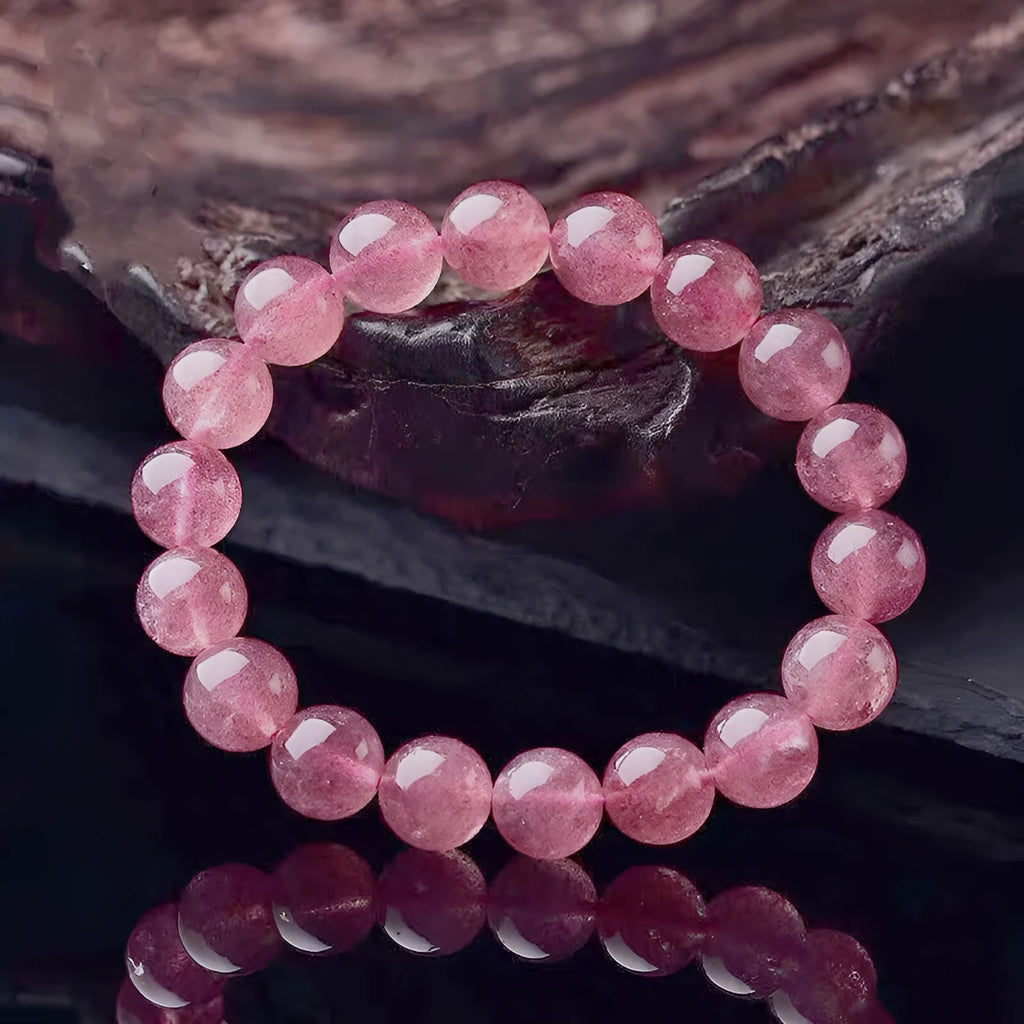Women's strawberry quartz crystal bracelet in polished pink beads on a white background.