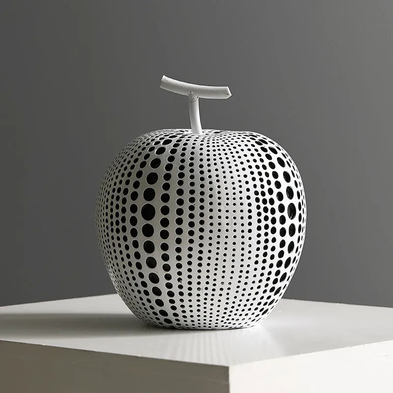 Decorative resin apple and pear crafts in white, orange, black, and blue on a shelf.