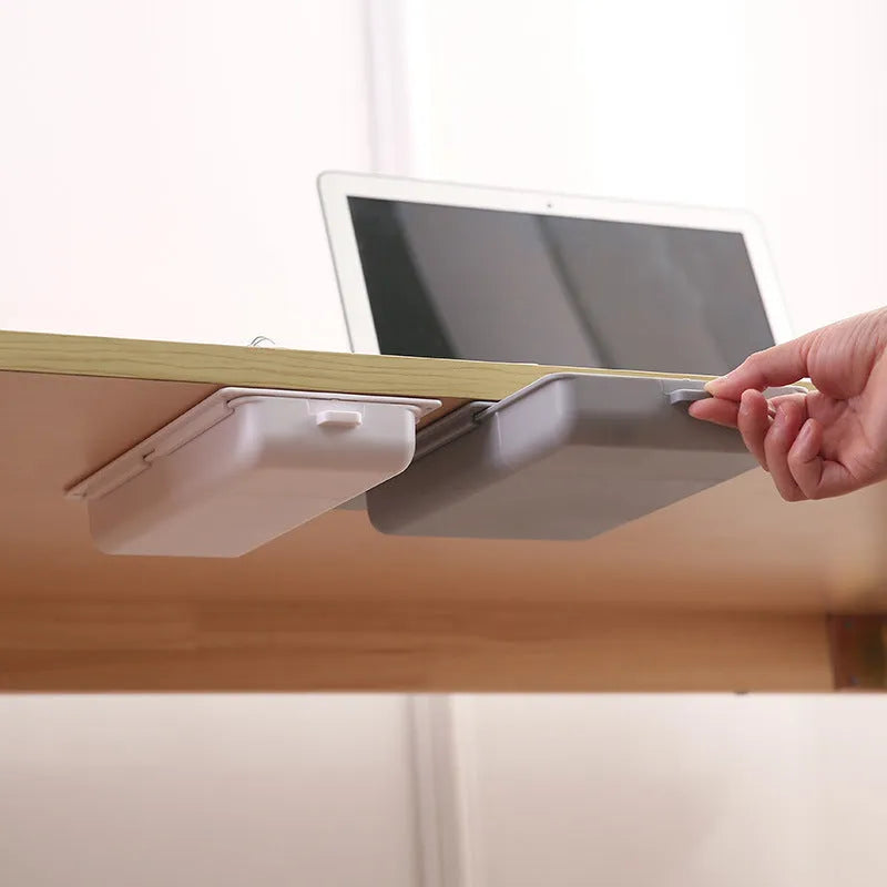 White plastic adhesive under-table storage box with a cover open, showing internal grid compartments.