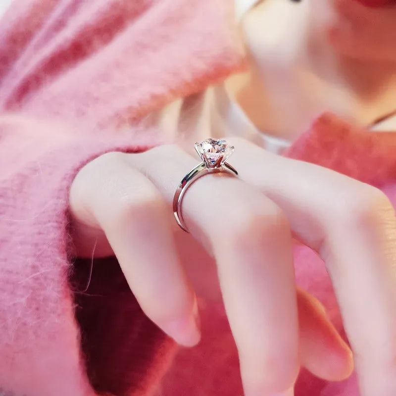 White gold plated geometric ring with a zircon stone in a six-claw setting on a finger.