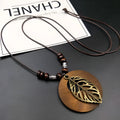 Vintage wooden leaf pendant necklace with beige fabric chain on a dark background.