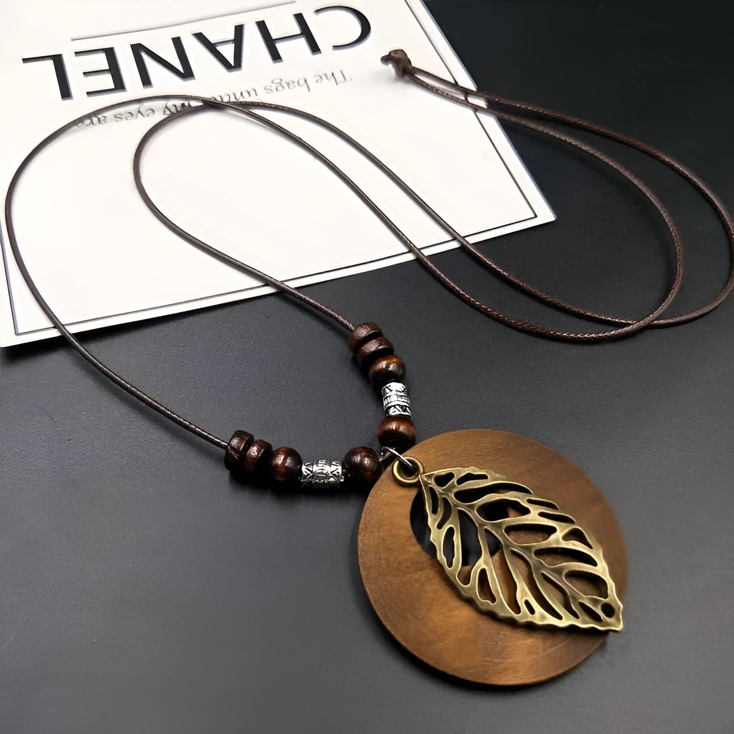 Vintage wooden leaf pendant necklace with beige fabric chain on a dark background.