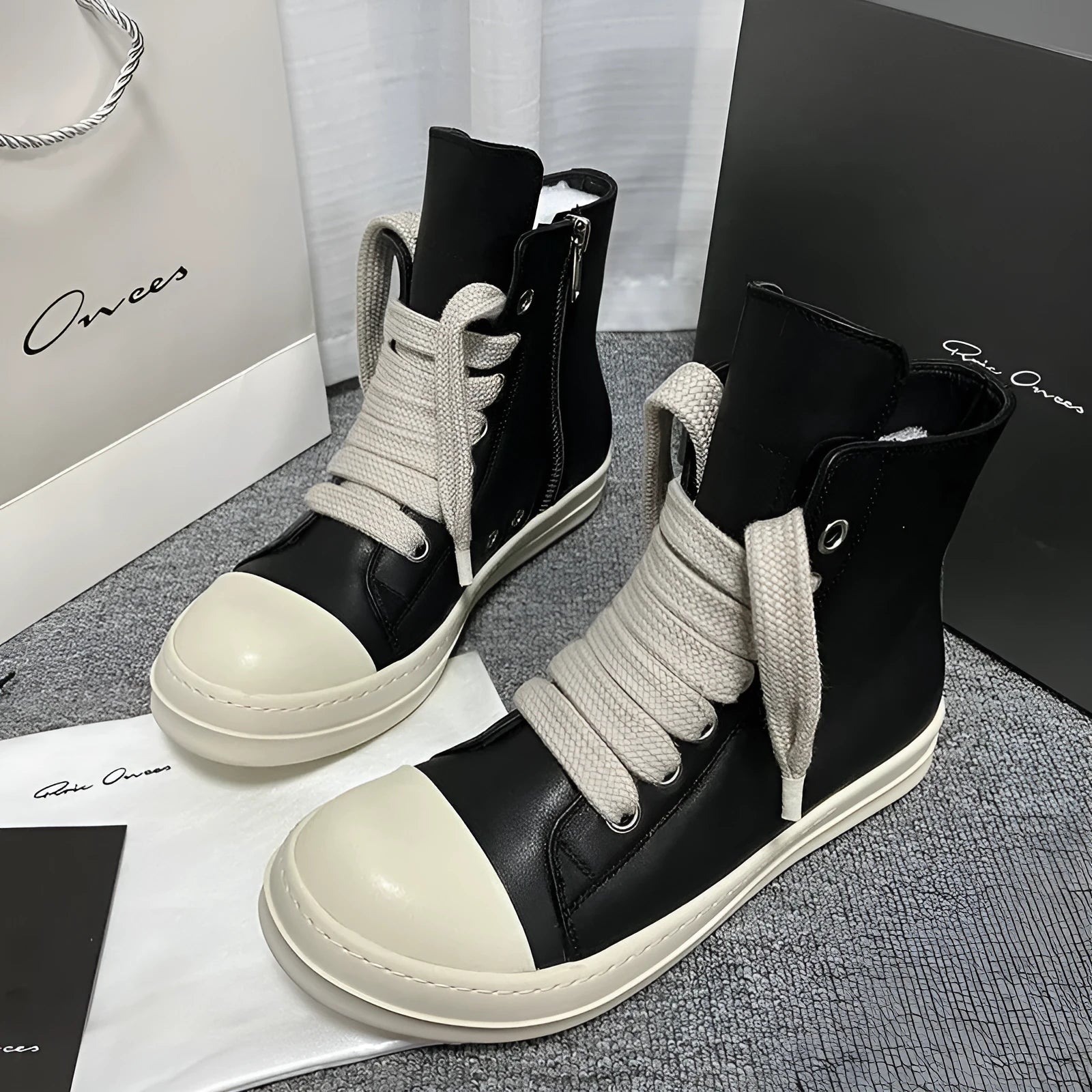 Men's and women's black high-top leather shoes with a side zipper and visible stitching on a round toe