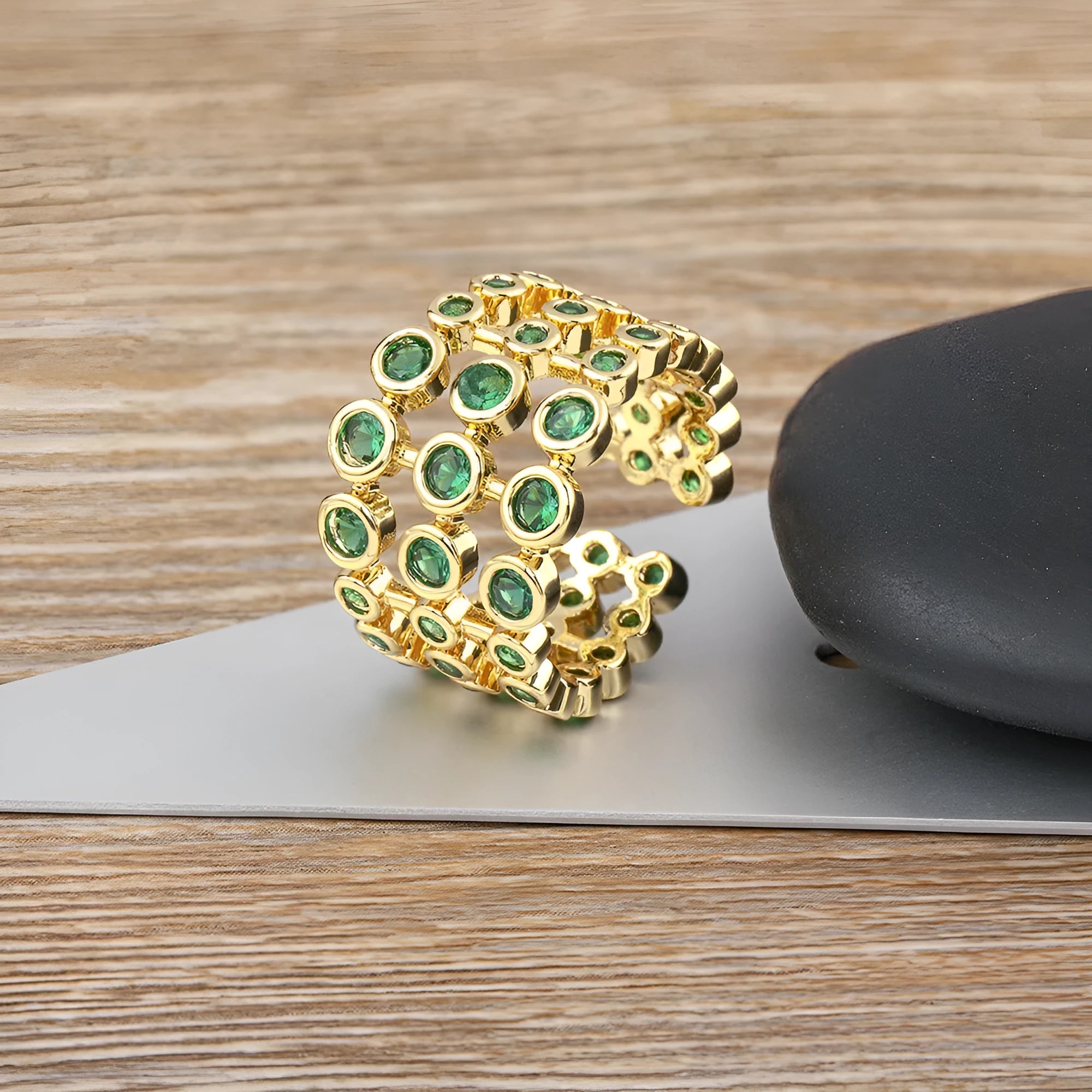Gold coloured wide band ring with green zircon stones, shown from the side.