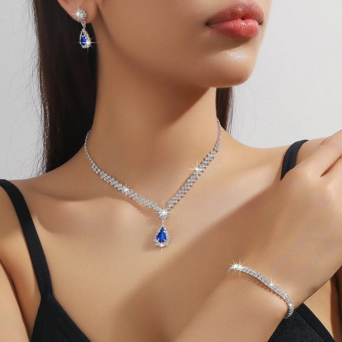 Women's claw chain necklace and drop rhinestone earrings set in blue on a white background.
