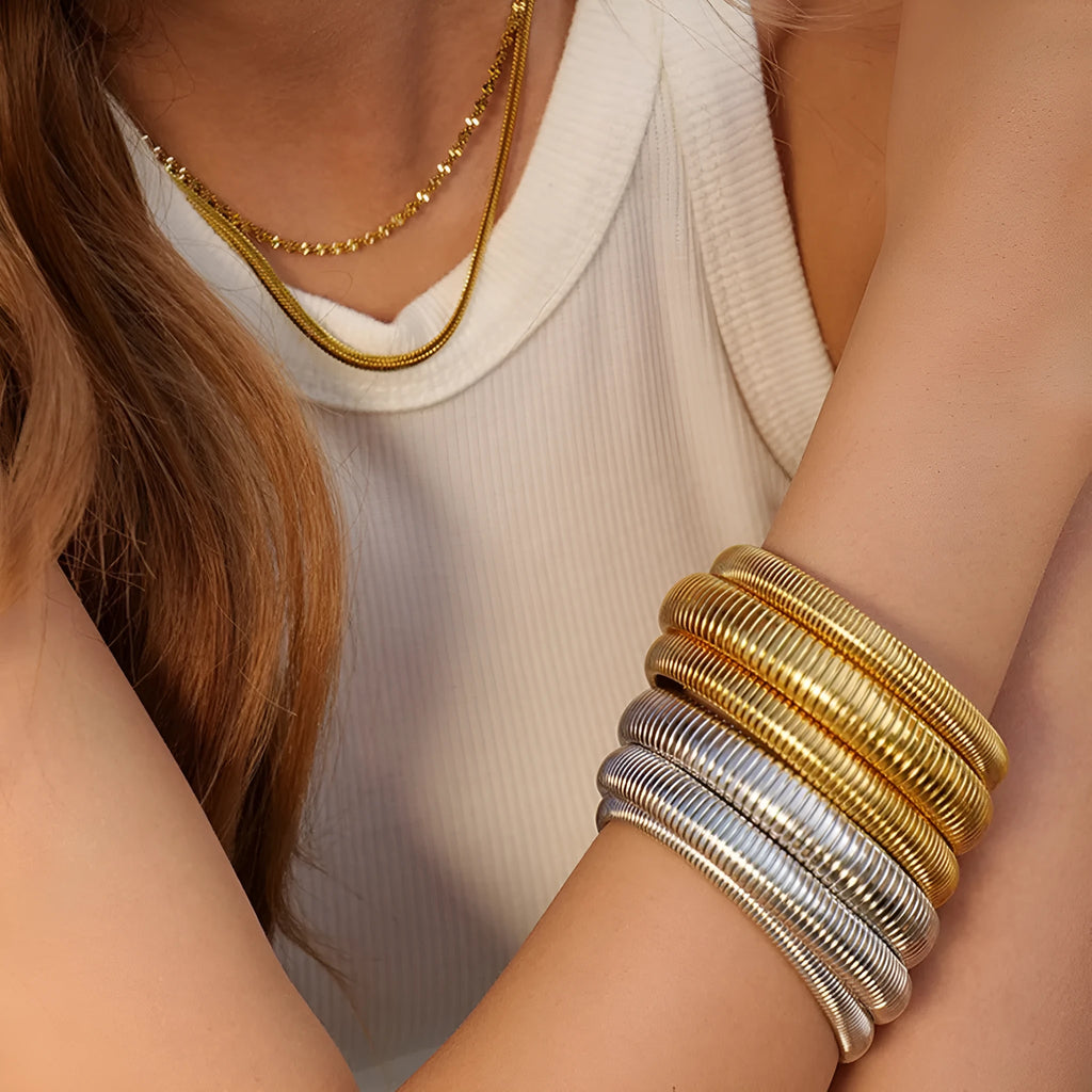 A gold women's elastic titanium steel bracelet with an exaggerated vertical stripe ring design, shown laid flat.