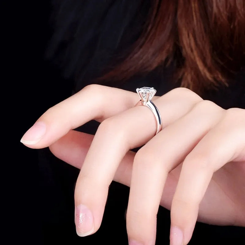 White gold plated geometric ring with a zircon stone in a six-claw setting on a finger.
