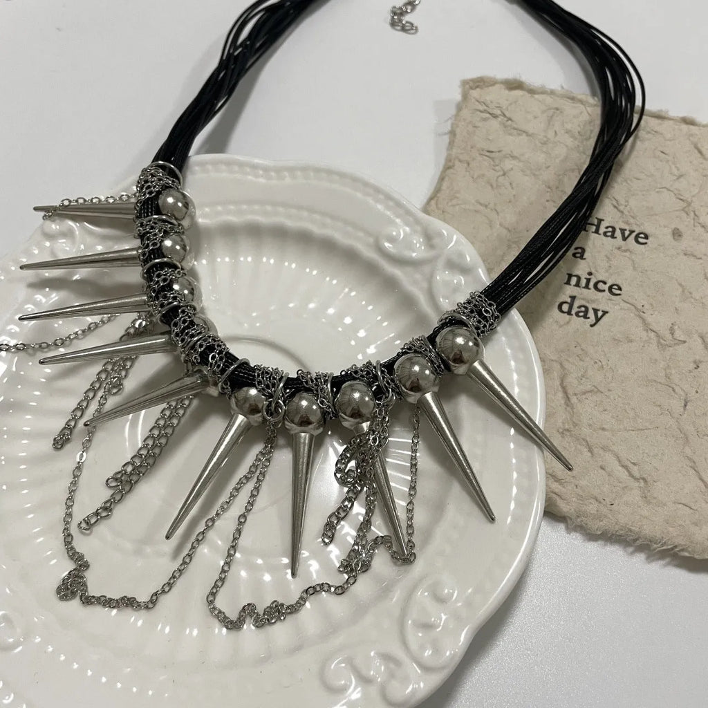 Leather necklace with winding round beads, metallic rivet details, and a long tassel in an electroplated finish.