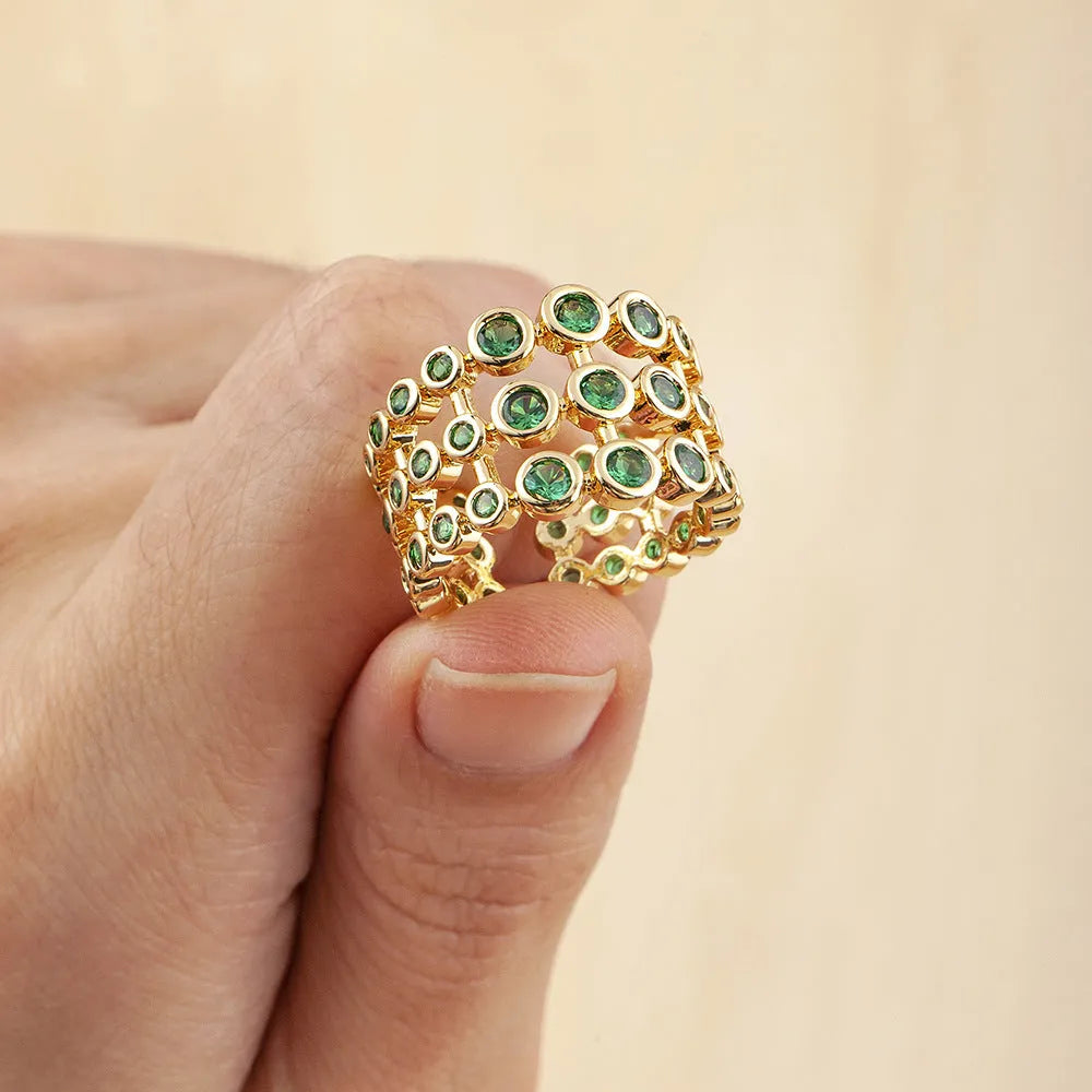 Gold coloured wide band ring with green zircon stones, shown from the side.
