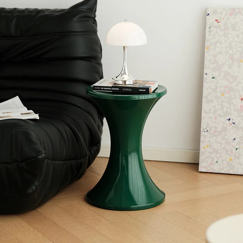 Hourglass-shaped plastic shoe changing stool in green colour on a wooden floor.