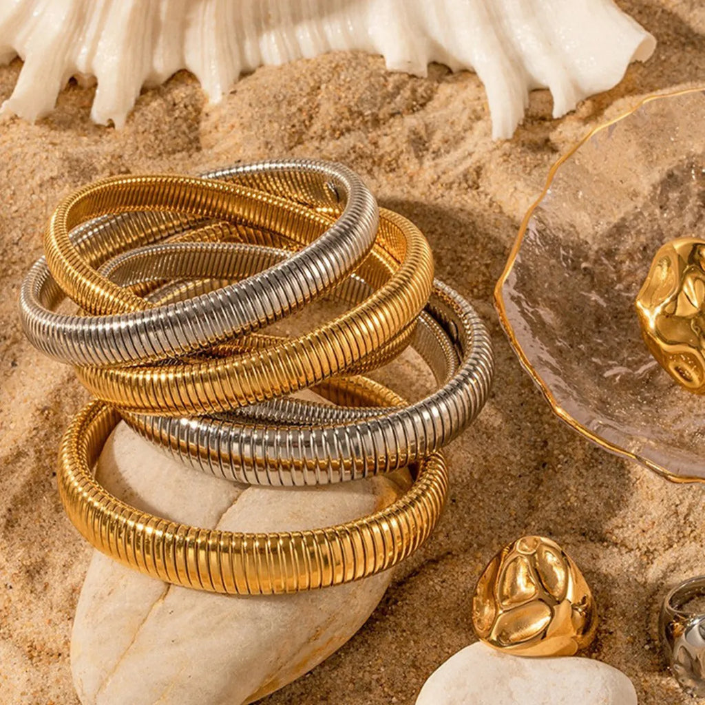 A gold women's elastic titanium steel bracelet with an exaggerated vertical stripe ring design, shown laid flat.