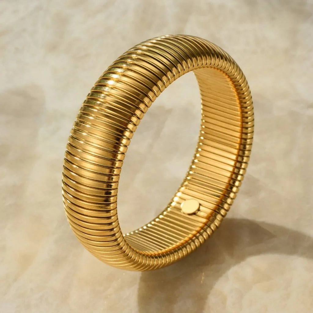 A gold women's elastic titanium steel bracelet with an exaggerated vertical stripe ring design, shown laid flat.