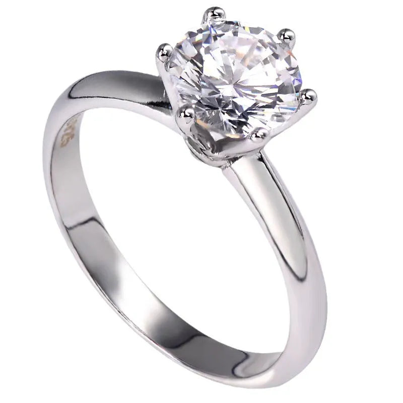 White gold plated geometric ring with a zircon stone in a six-claw setting on a finger.