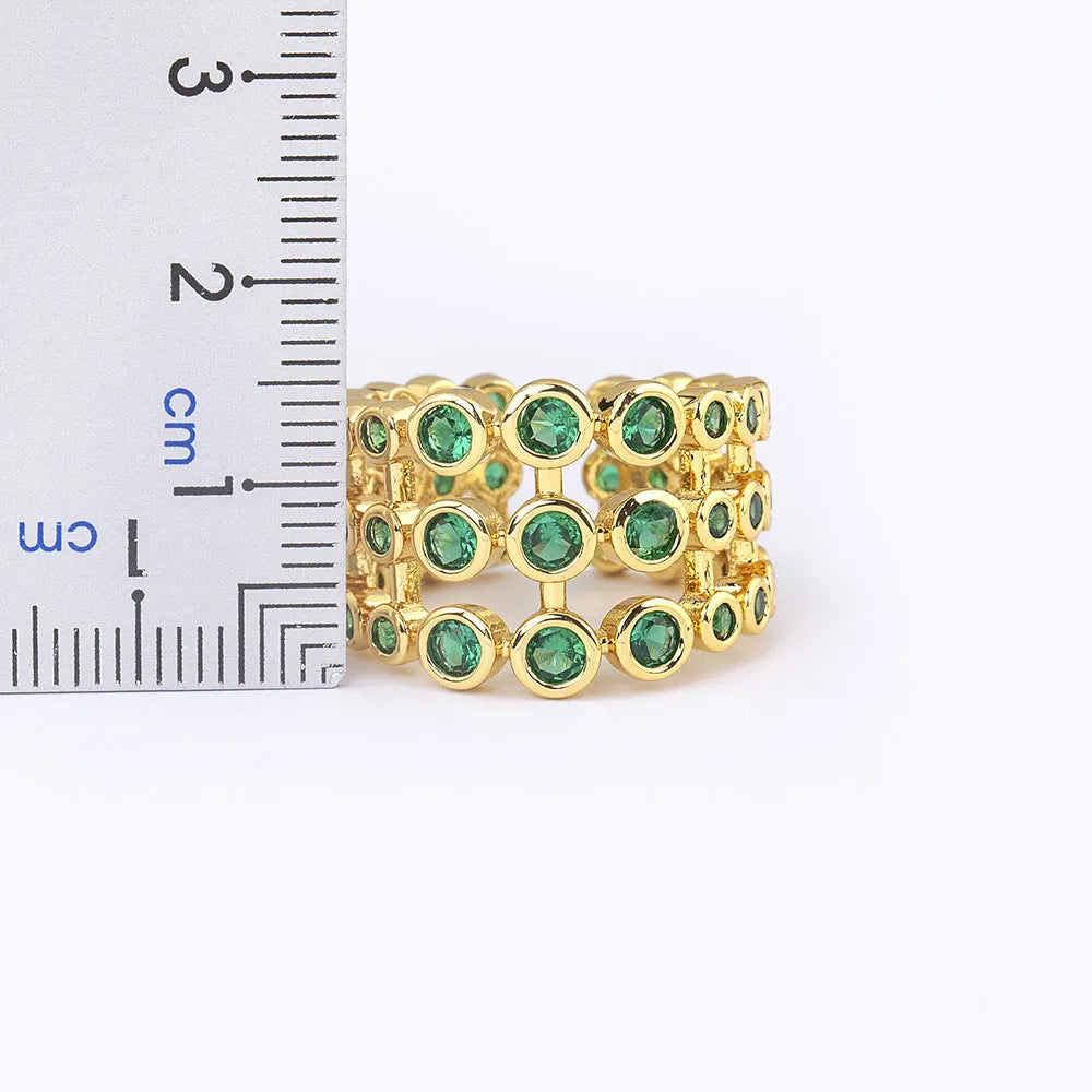Gold coloured wide band ring with green zircon stones, shown from the side.