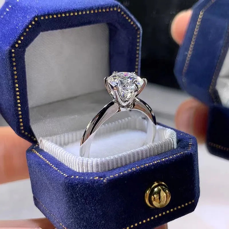 White gold plated geometric ring with a zircon stone in a six-claw setting on a finger.