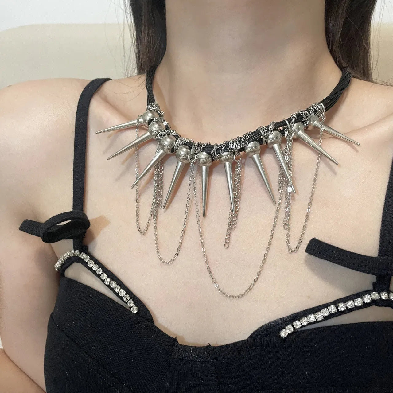 Leather necklace with winding round beads, metallic rivet details, and a long tassel in an electroplated finish.