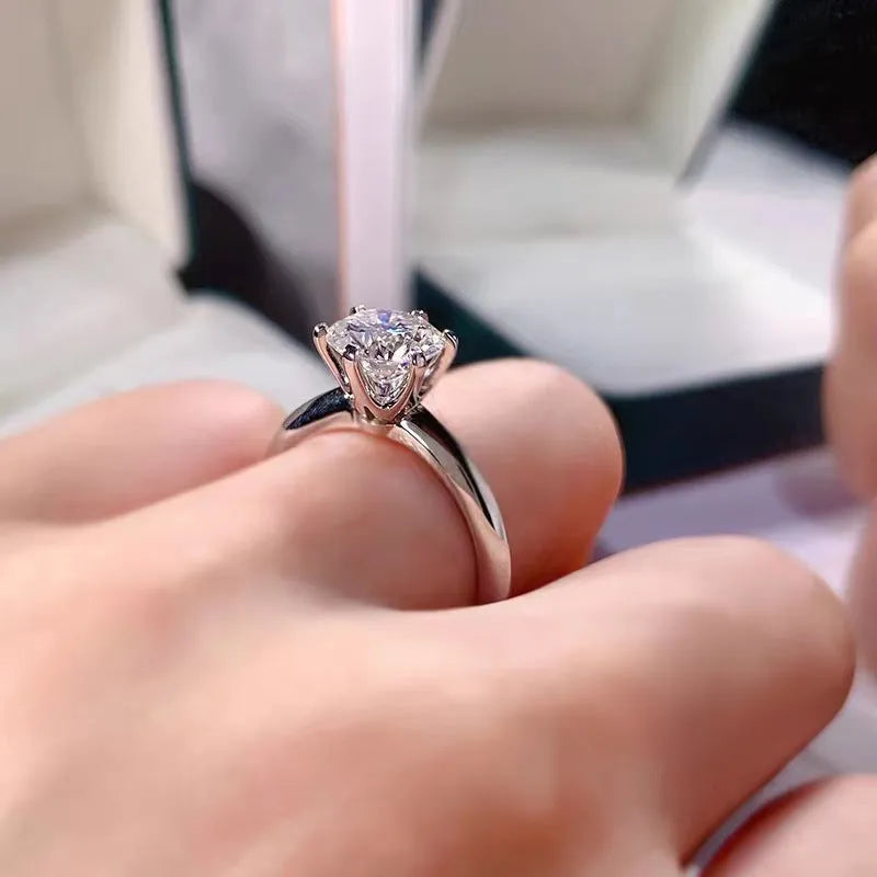 White gold plated geometric ring with a zircon stone in a six-claw setting on a finger.