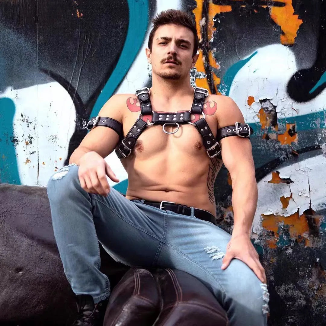 Black leather chest strap for men with metal buckle and rivet details on a mannequin.