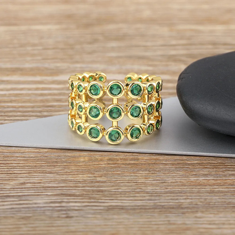 Gold coloured wide band ring with green zircon stones, shown from the side.