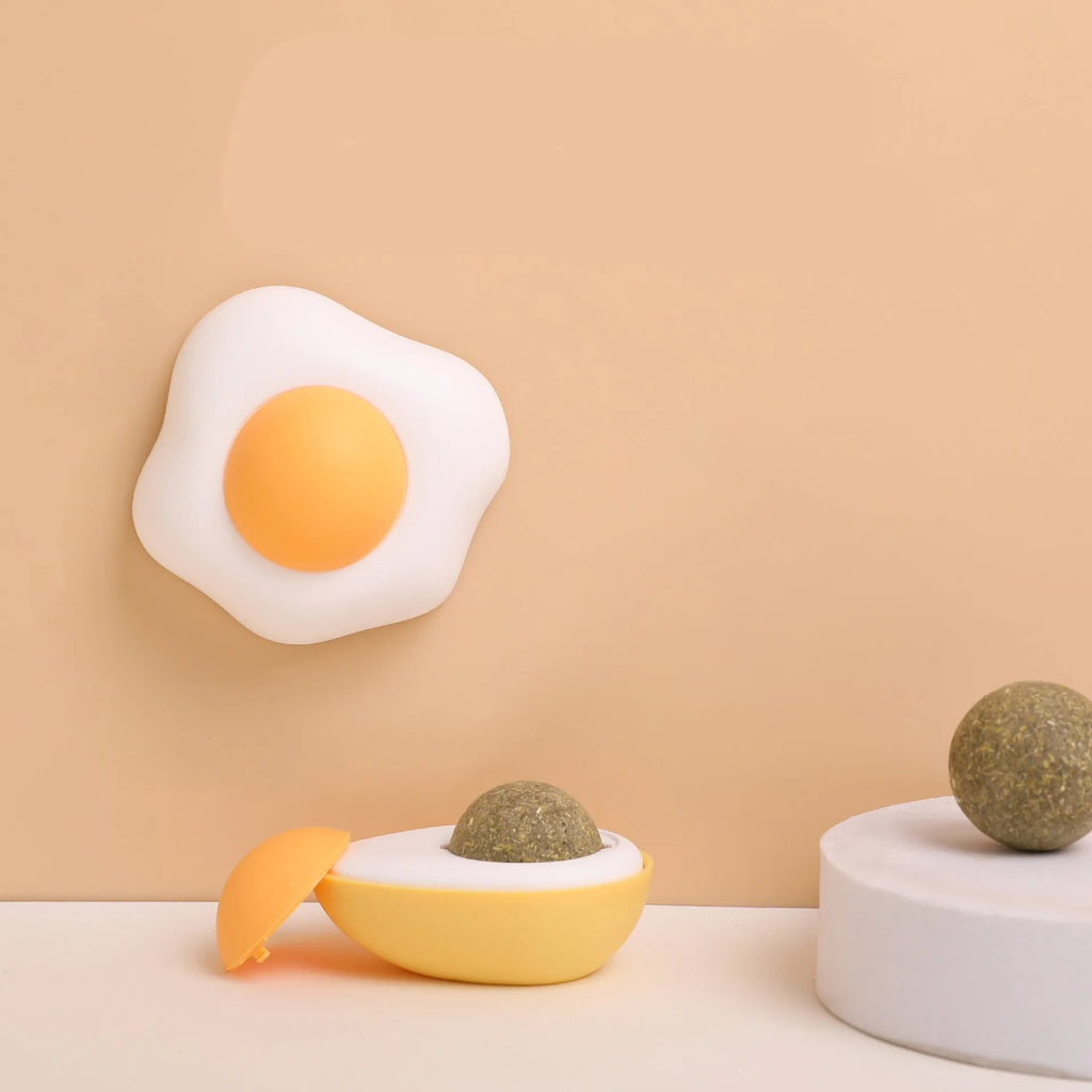 Soft plush catnip ball toy with adhesive base sticking to a wall for interactive feline play