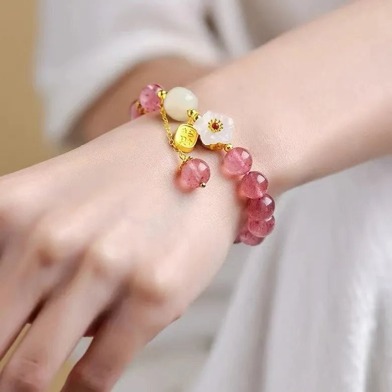 Handmade strawberry quartz crystal bracelet with peach blossom design on a wrist.