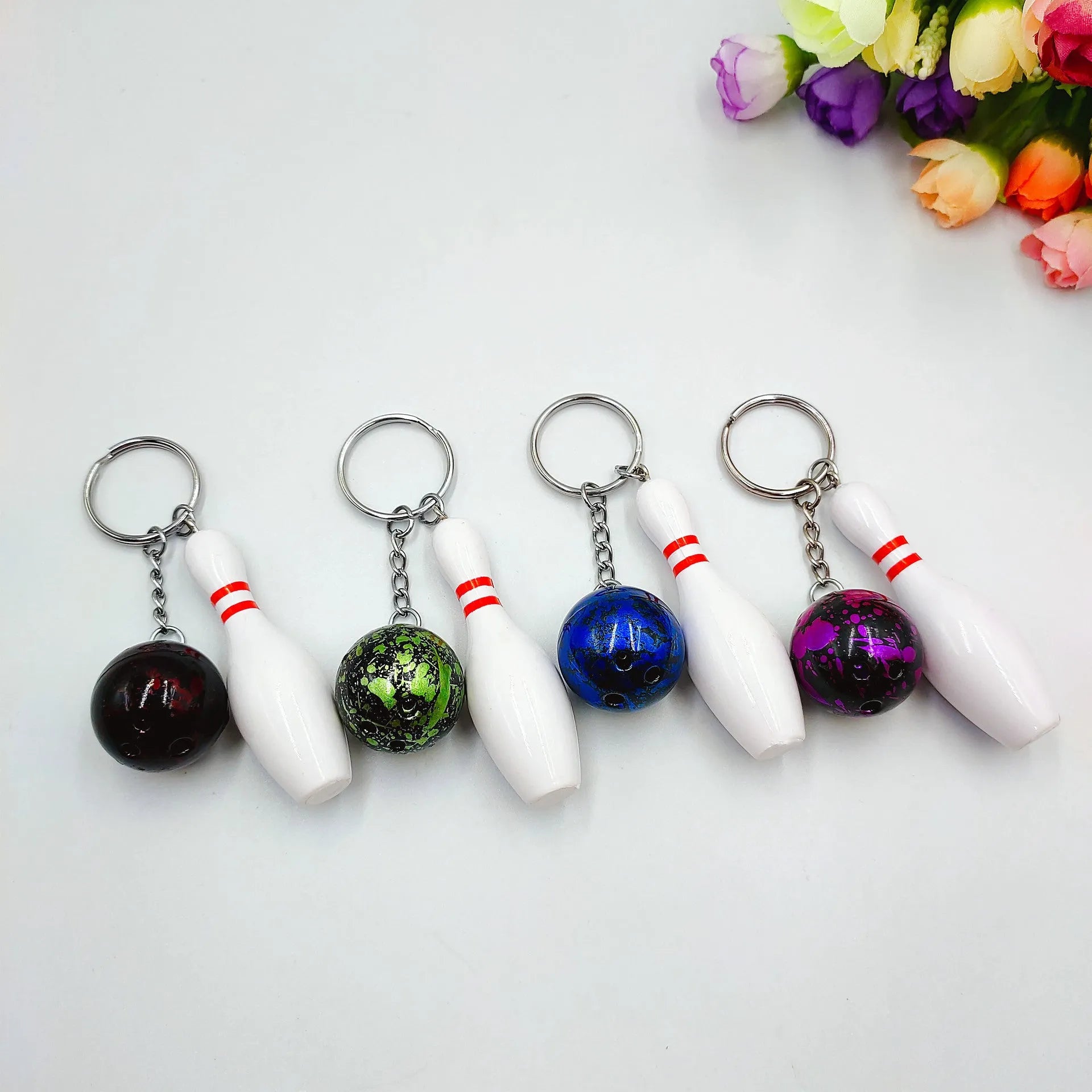 Miniature dark red bowling ball keychain on a metal ring with blue, purple, and green colour options shown