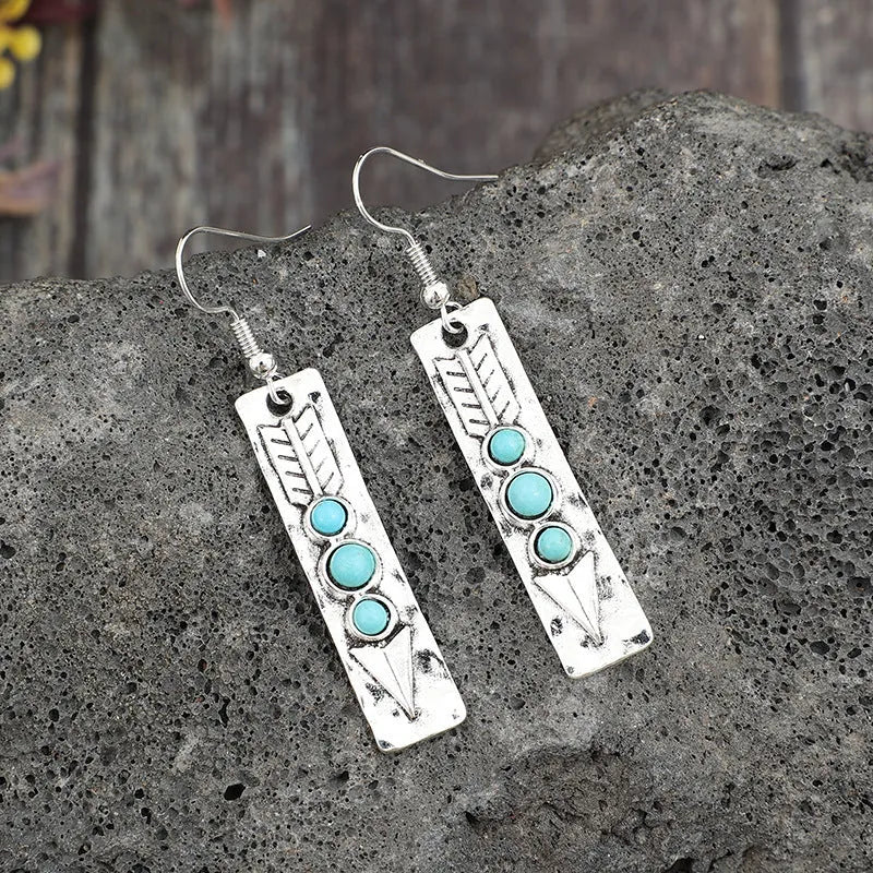 Long silver geometric earrings with a blue turquoise stone detail on a white background.