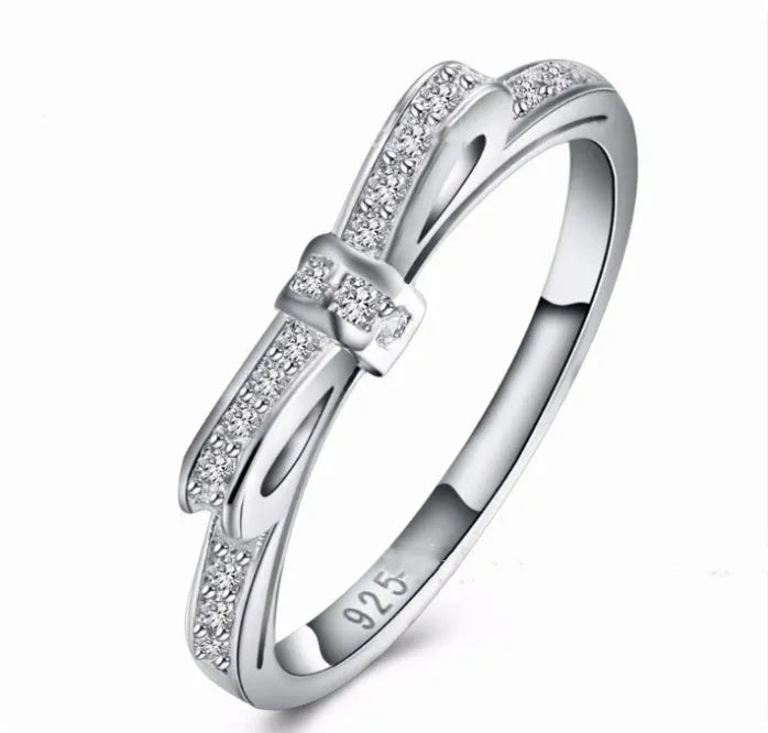 Silver couple ring with a bow-shaped centre decorated with sparkling rhinestone crystals on a finger.